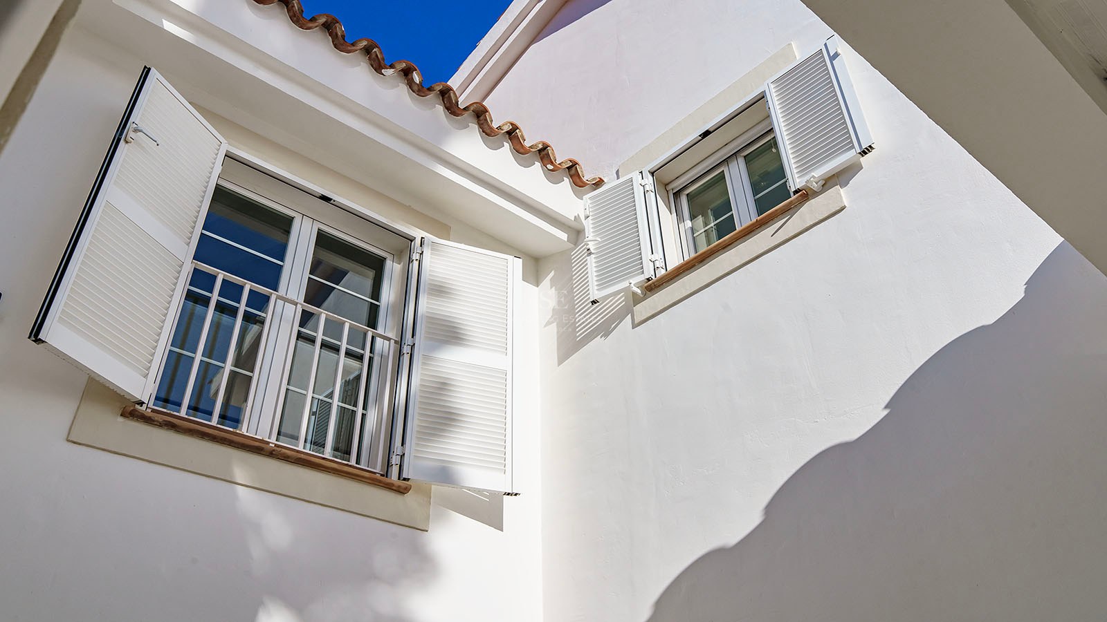 Détail d'une façade blanche avec volets majorquins, tuiles en terre cuite et appuis de fenêtre en pierre.