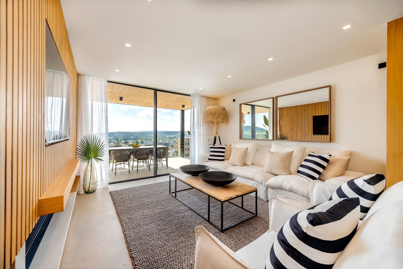 Salón contemporáneo con paneles de roble, sofás blancos y grandes ventanales que dan a una terraza con vistas.