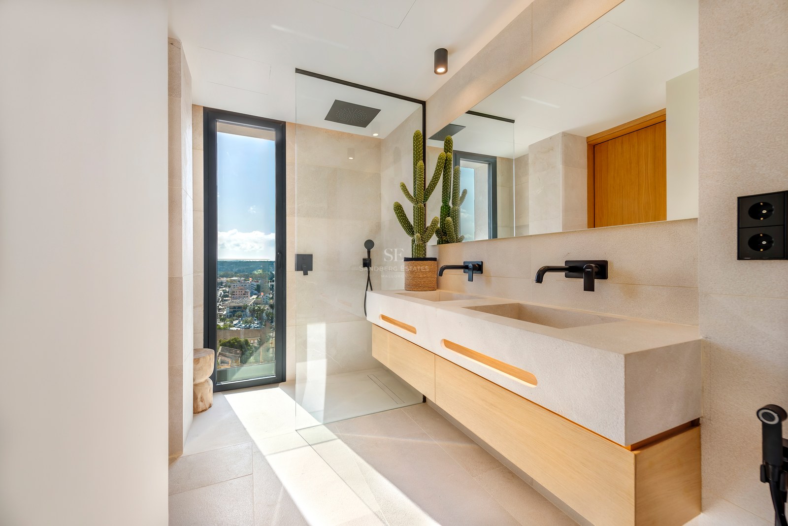 Baño contemporáneo con lavabo doble de piedra, ducha de cristal y ventanal con vistas a la costa.