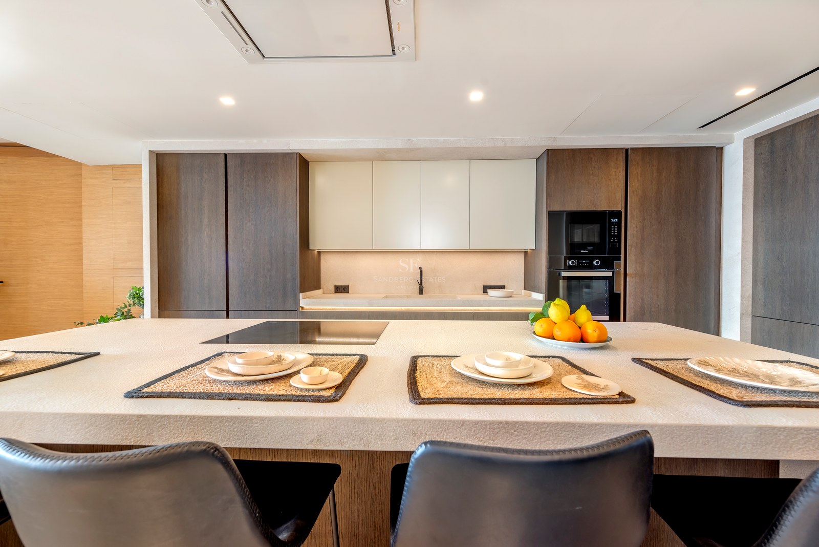 Cocina moderna con una gran isla de piedra texturizada, armarios de madera oscura y electrodomésticos integrados.