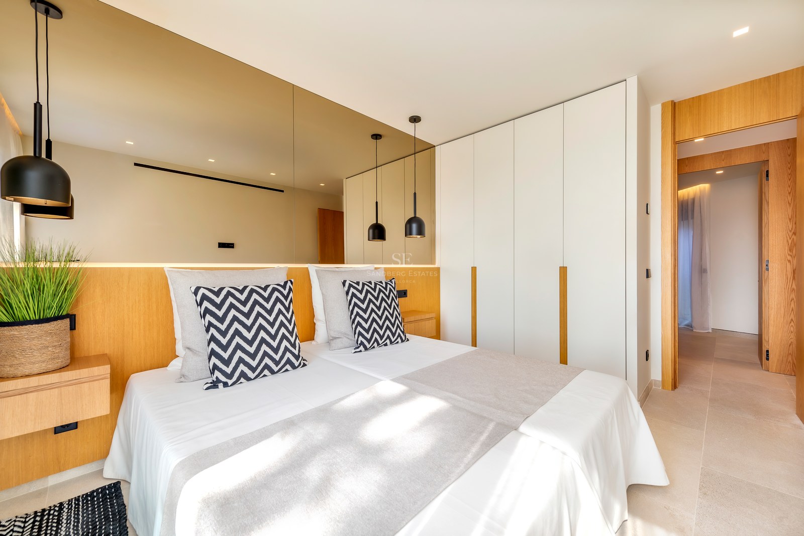 Dormitorio contemporáneo con cabecero de madera integrado, pared de espejos y armarios empotrados blancos.