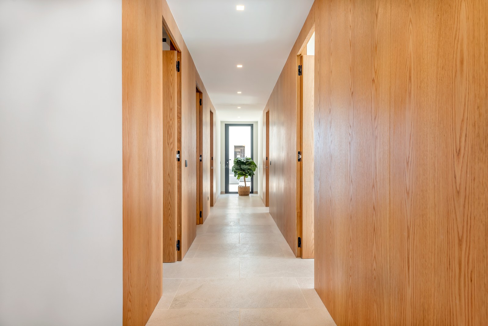Pasillo moderno con paneles de madera de roble de suelo a techo y puertas integradas bajo una iluminación cálida.