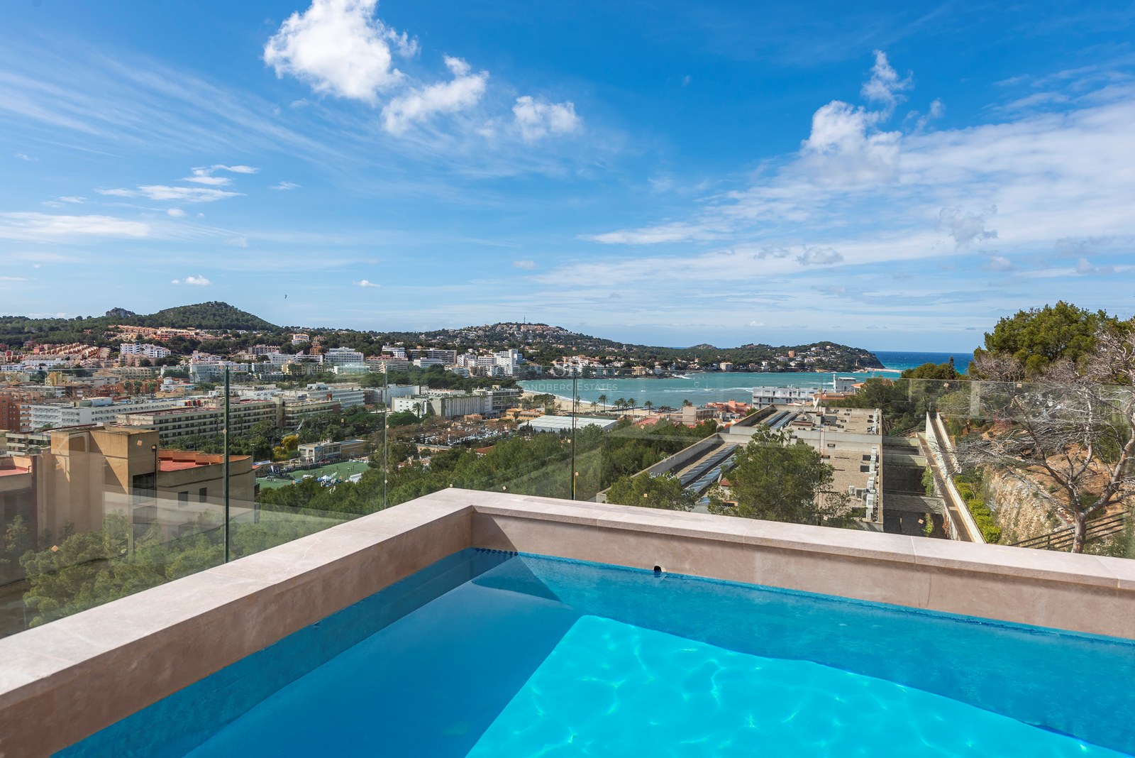 Piscina en la azotea con barandillas de cristal con vistas a un pueblo costero mediterráneo y al mar.
