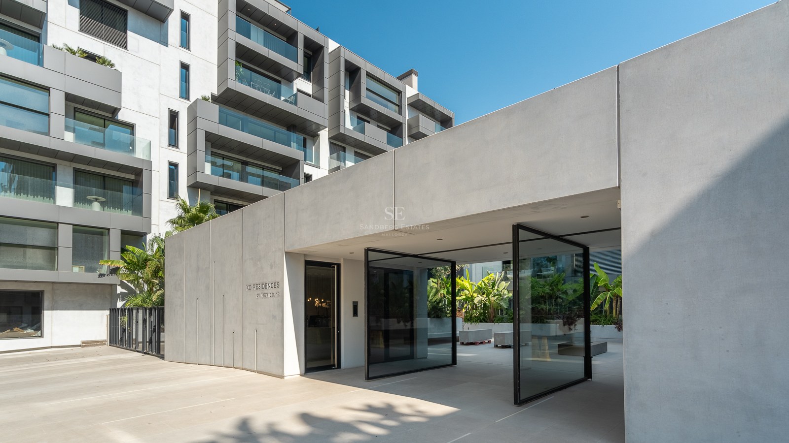 Architectural concrete entrance with oversized glass pivot doors leading into a luxury modern apartment complex.