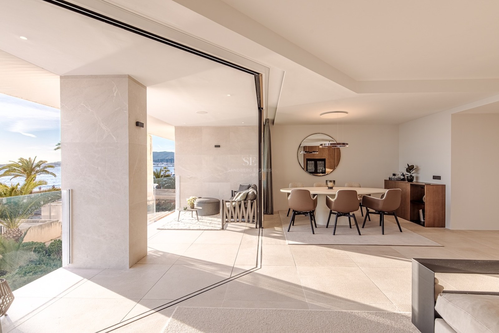 Contemporary dining room with beige stone floors and large sliding glass doors opening to a terrace with sea views.
