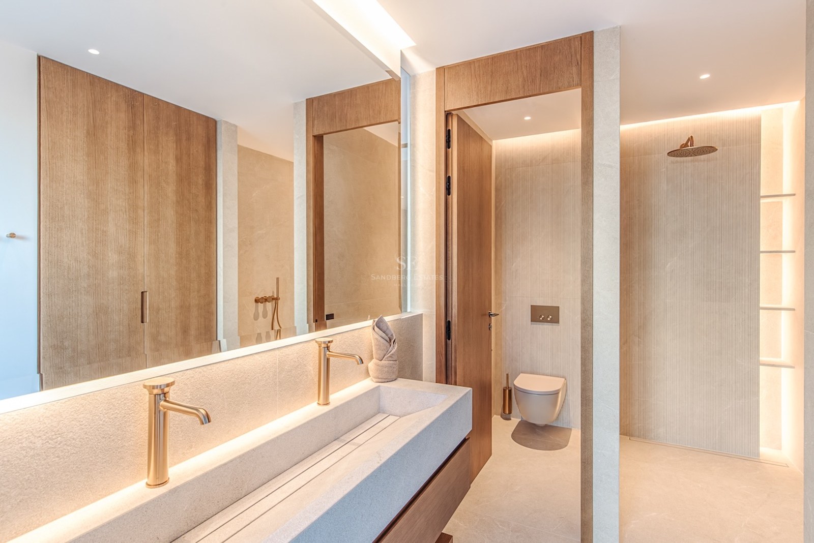 Modern bathroom featuring a long stone double sink, gold faucets, a walk-in shower, and wood paneling.