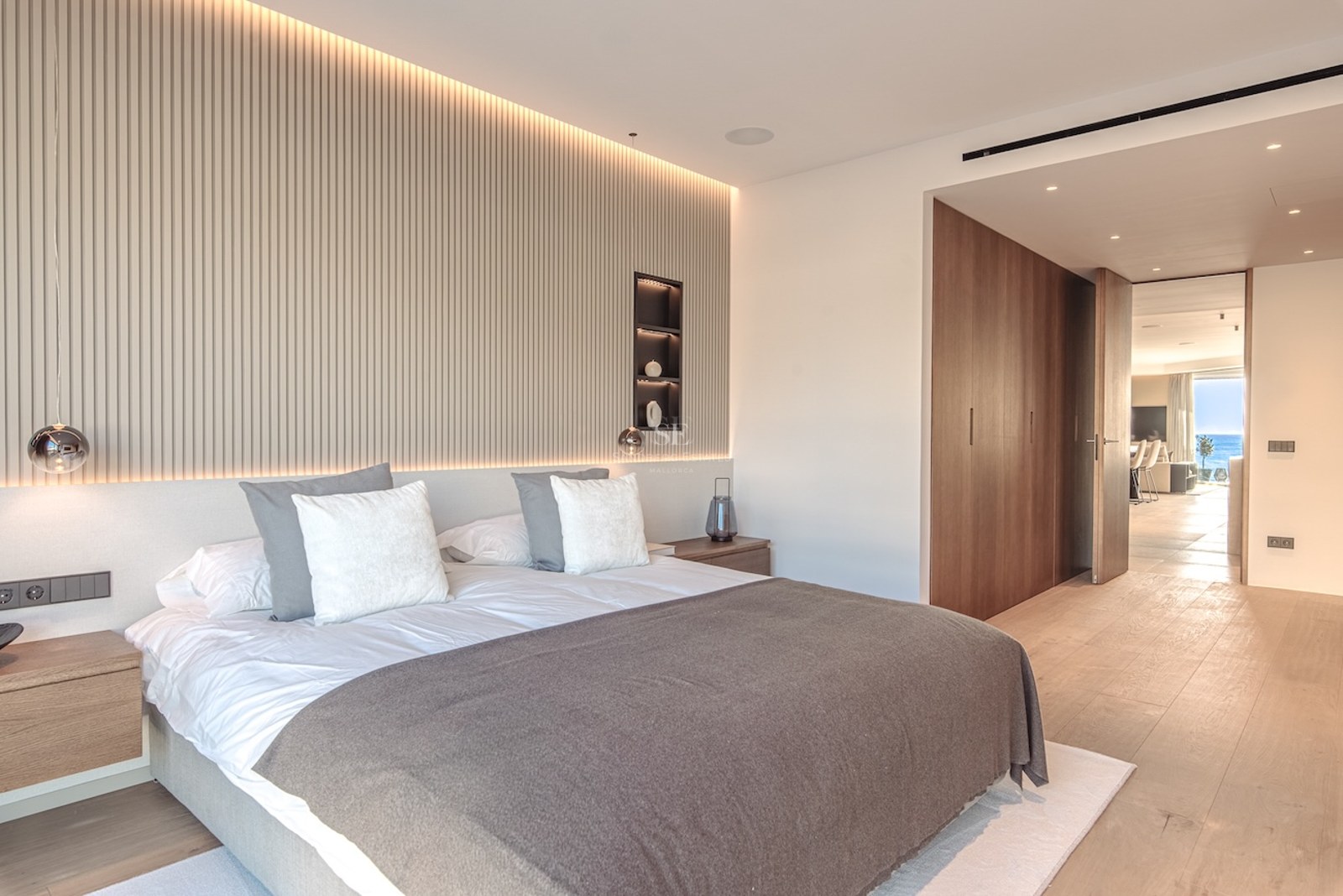 Luxury bedroom featuring a slatted wood accent wall, indirect LED lighting, oak floors, and minimalist furniture.