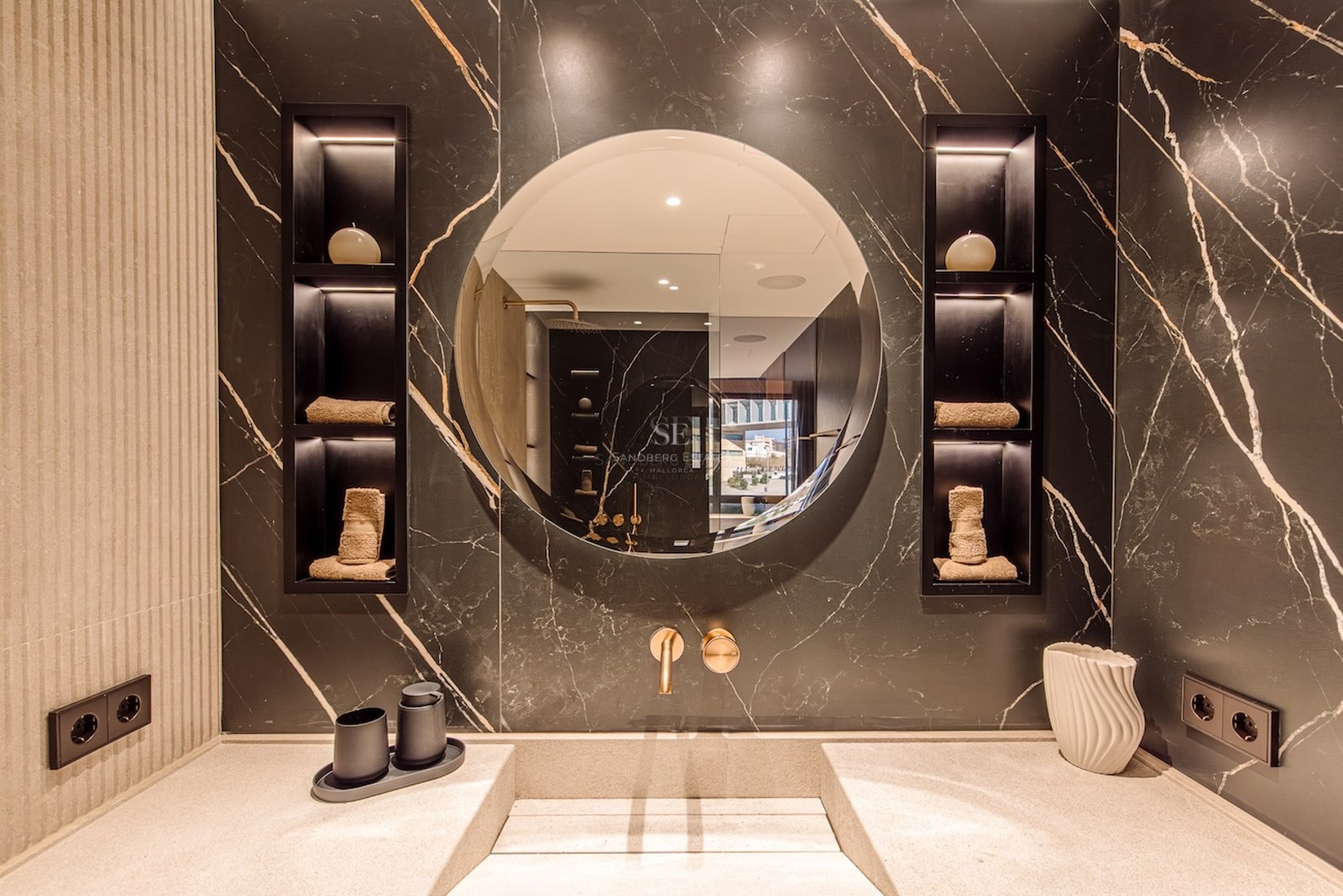 Modern bathroom vanity featuring a round mirror, black marble wall with gold veins, and integrated stone sink.