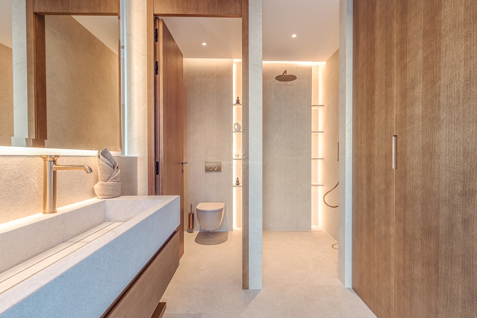 Modern bathroom featuring a stone trough sink, brass fixtures, and a walk-in shower with warm LED accent lighting.