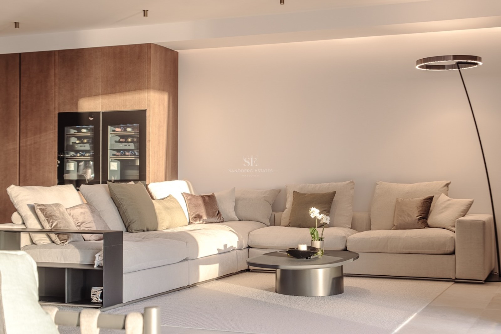 Modern living room featuring a large beige modular sofa, integrated glass wine fridge, and designer halo floor lamp.