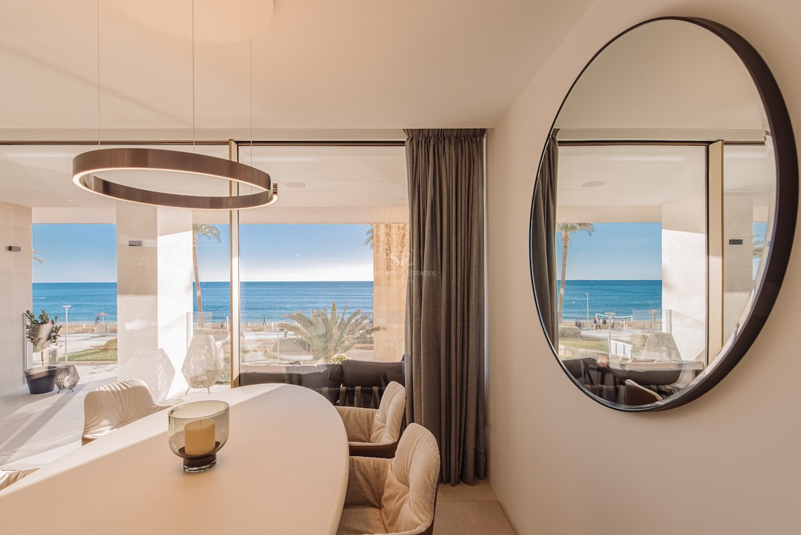 Luxury dining room featuring a white oval table and floor-to-ceiling windows overlooking the Mediterranean beach.