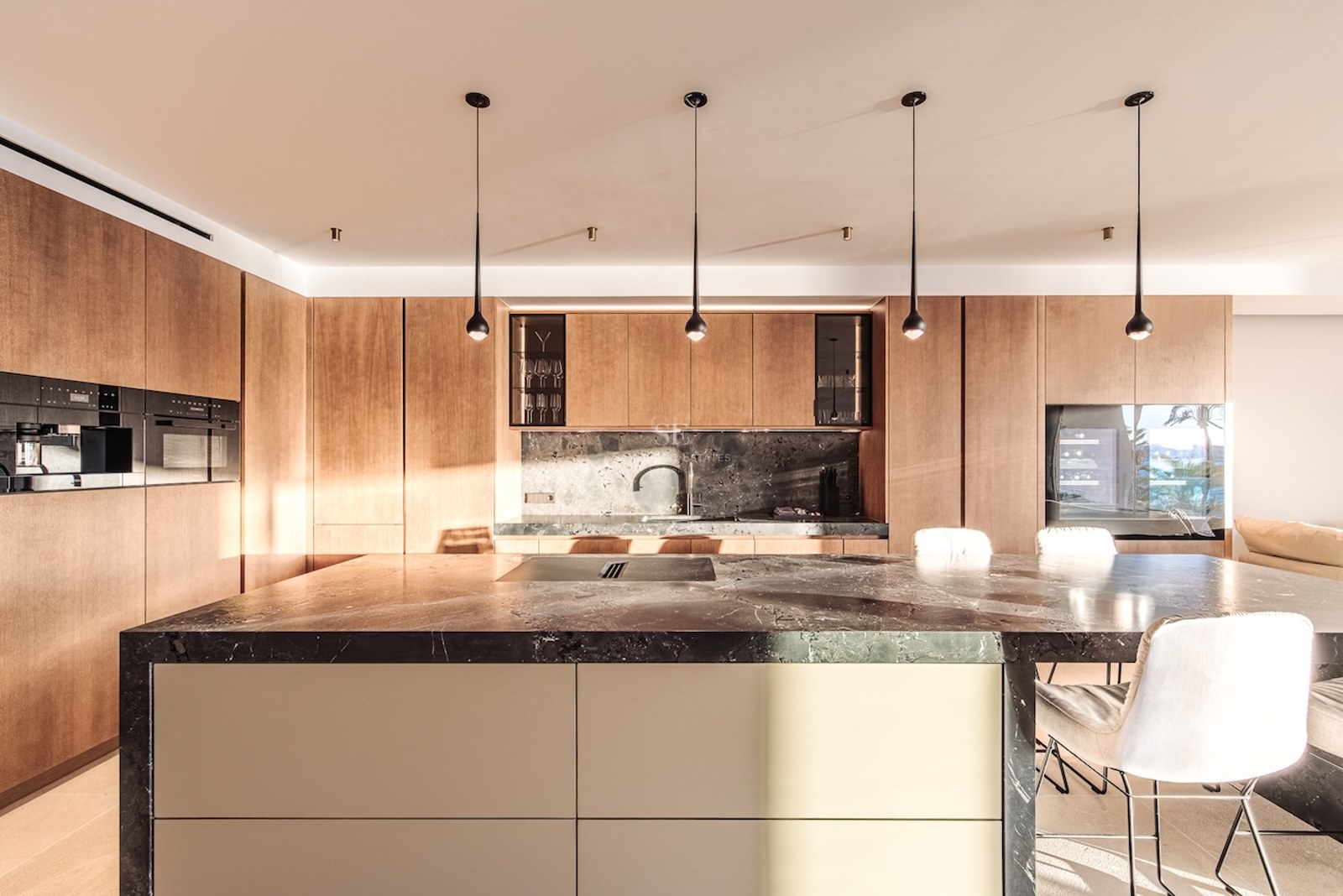 Modern kitchen featuring a large dark marble island with seating, natural wood cabinets, and minimalist pendant lights.