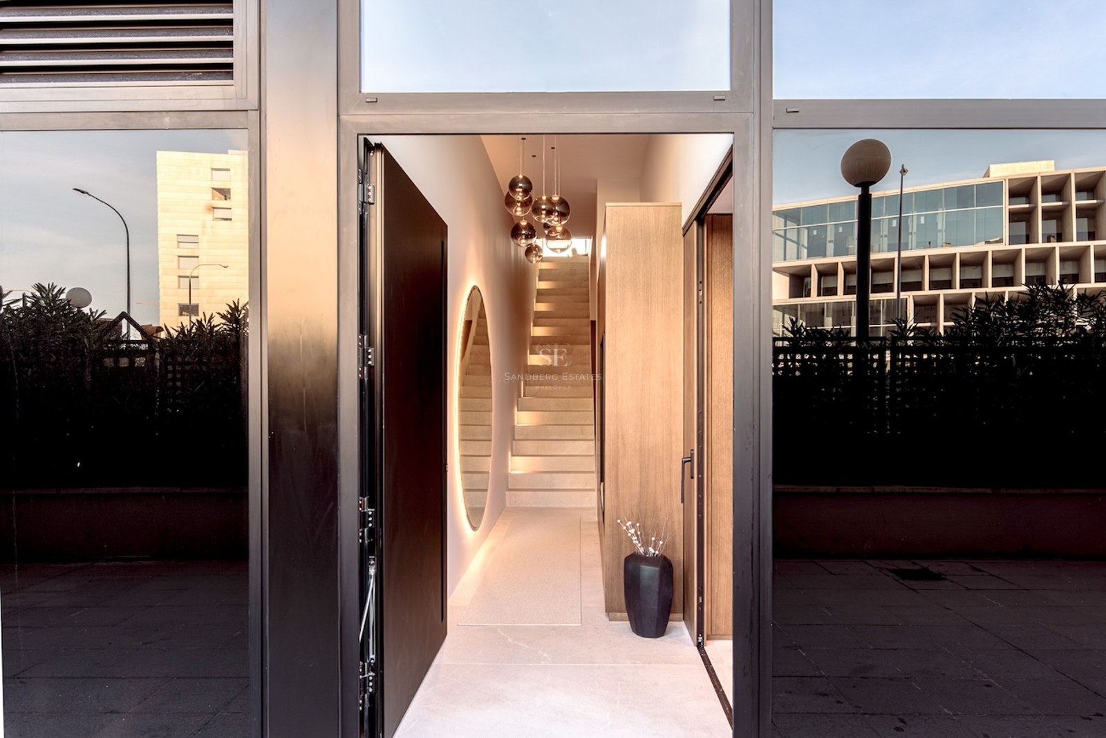 View through an open black door into a modern hallway featuring a stone staircase and designer glass pendant lights.