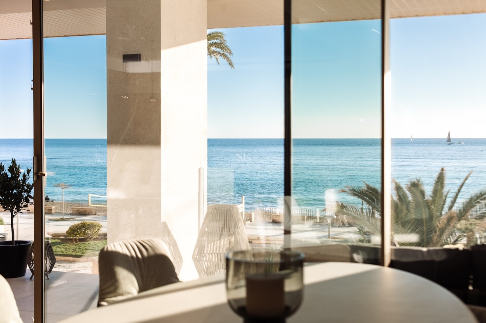 Mediterranean Sea view through floor-to-ceiling glass doors from a modern interior with a covered terrace.