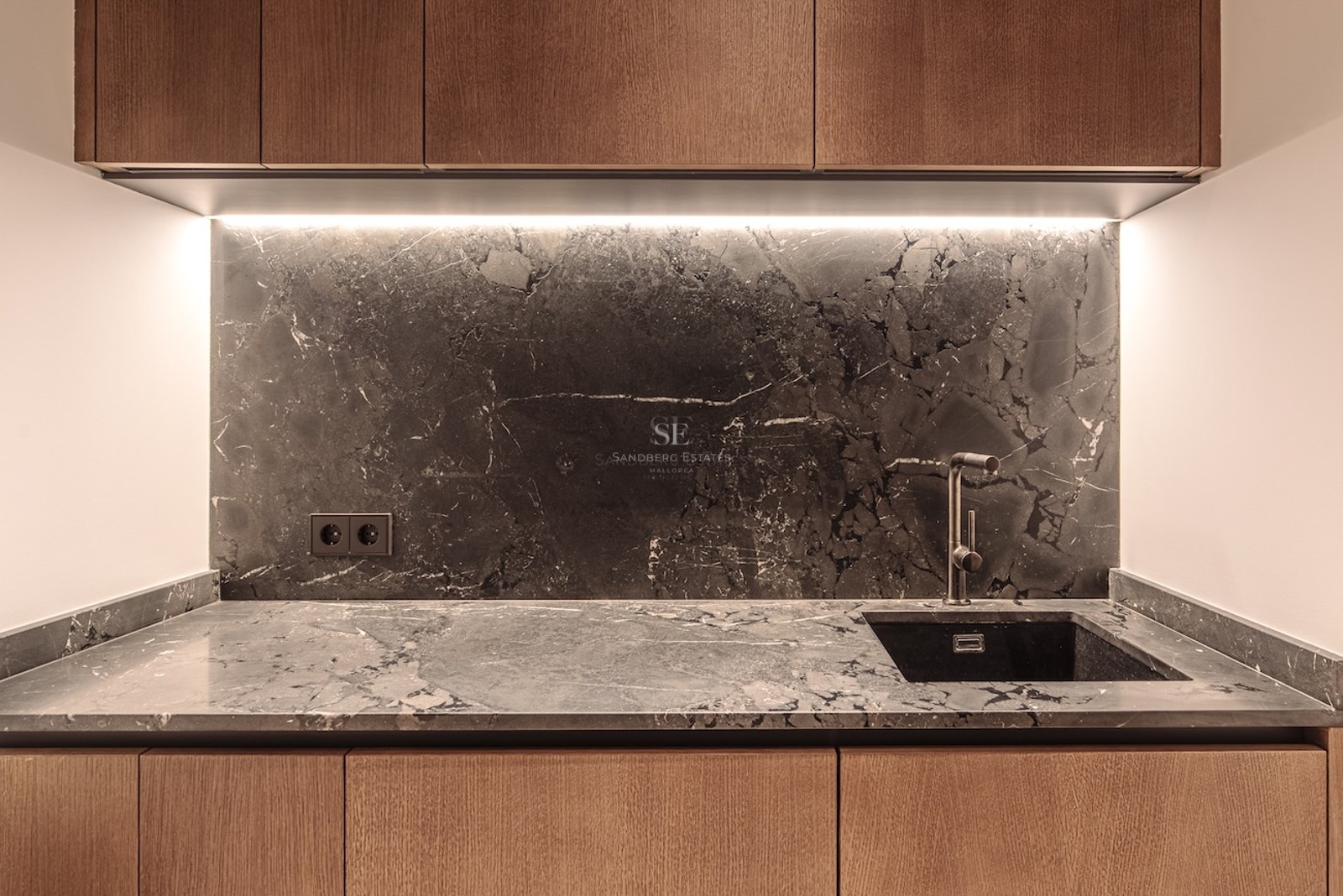 Close-up of a kitchen featuring dark marble backsplash, wooden cabinets, and integrated LED lighting.