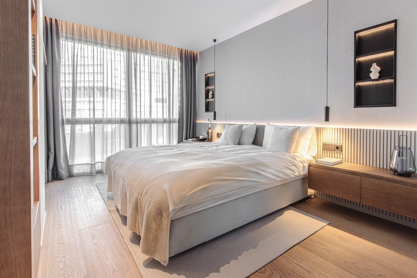 Modern bedroom featuring oak floors, floor-to-ceiling windows, and a wood-slatted headboard with integrated LED lighting.