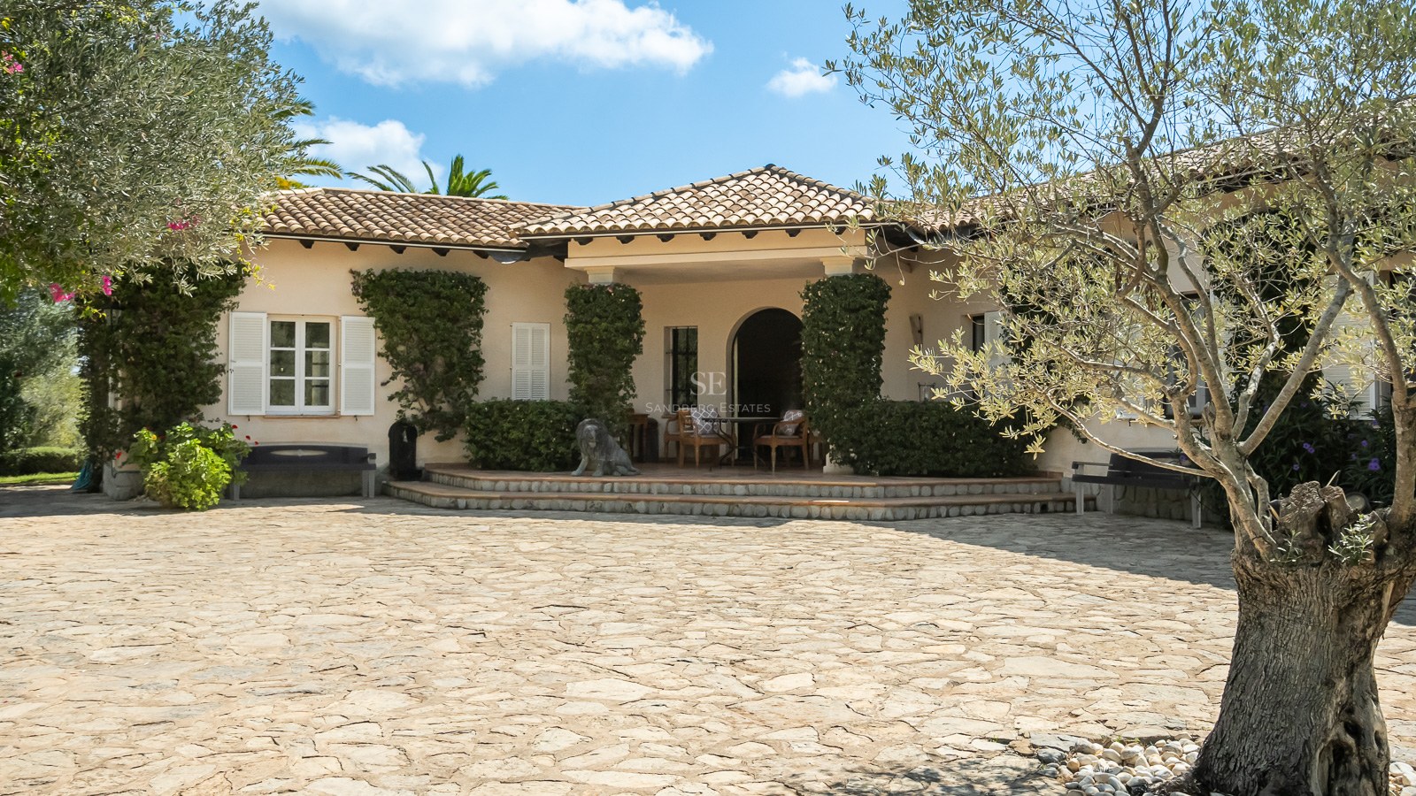 Cremefarbene mediterrane Villa mit Terrakotta-Dachziegeln, weißen Fensterläden und einem großen Naturstein-Hof.