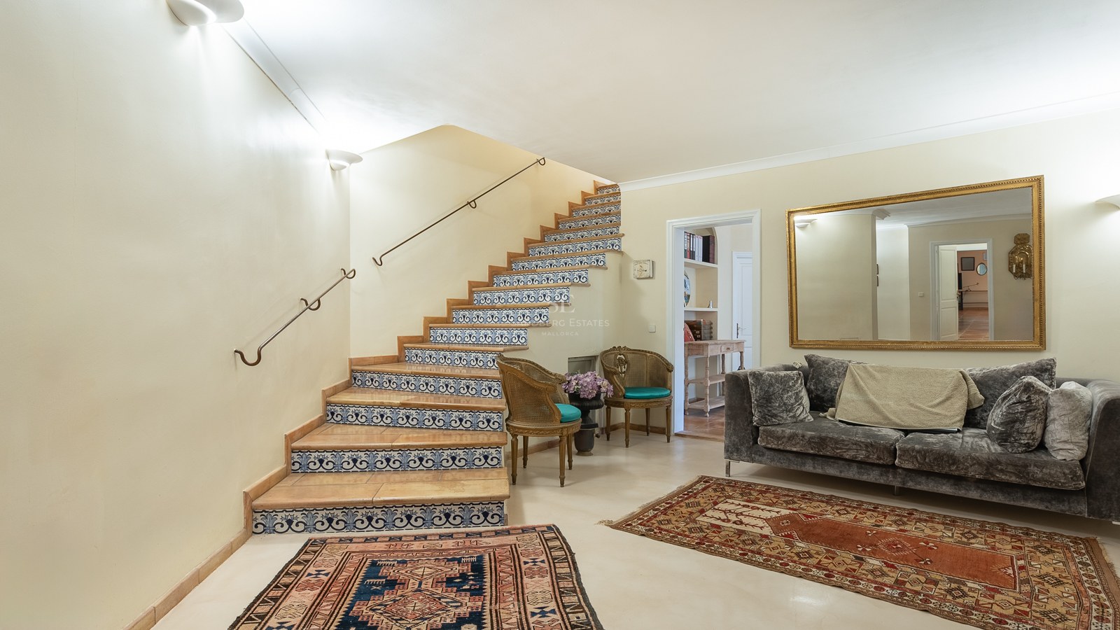 Innenansicht einer Eingangshalle mit einer Treppe mit blau-weißen Fliesen, Samtsofa und Orientteppichen.