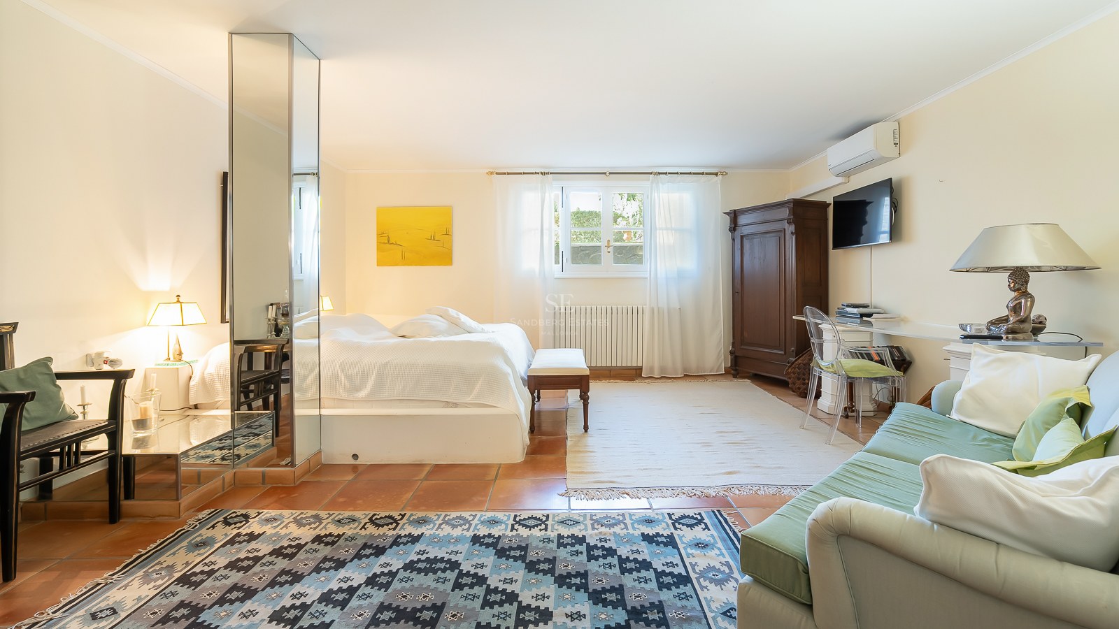 Geräumiges Schlafzimmer mit Terrakottaboden, Spiegelsäule, weißem Bettzeug, antikem Schrank und Sitzecke.