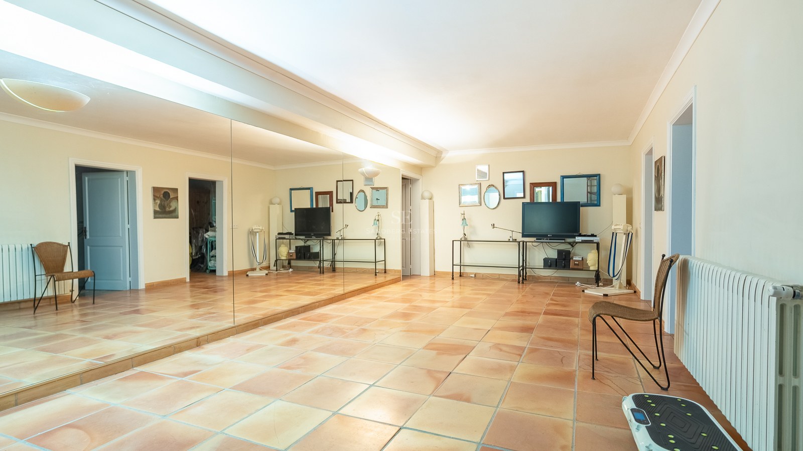 Großer Raum mit Terrakottafliesen, einer kompletten Spiegelwand und Fitnessgeräten in einer mediterranen Villa.