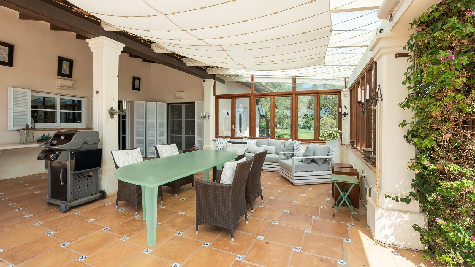 Überdachte Terrasse mit Terrakottafliesen, Esstisch, Loungebereich und Grill unter einer Markise.