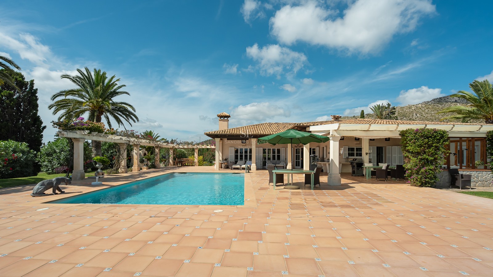 Großer rechteckiger Pool, umgeben von einer Terrakotta-Terrasse und einer weißen Villa unter blauem Himmel.