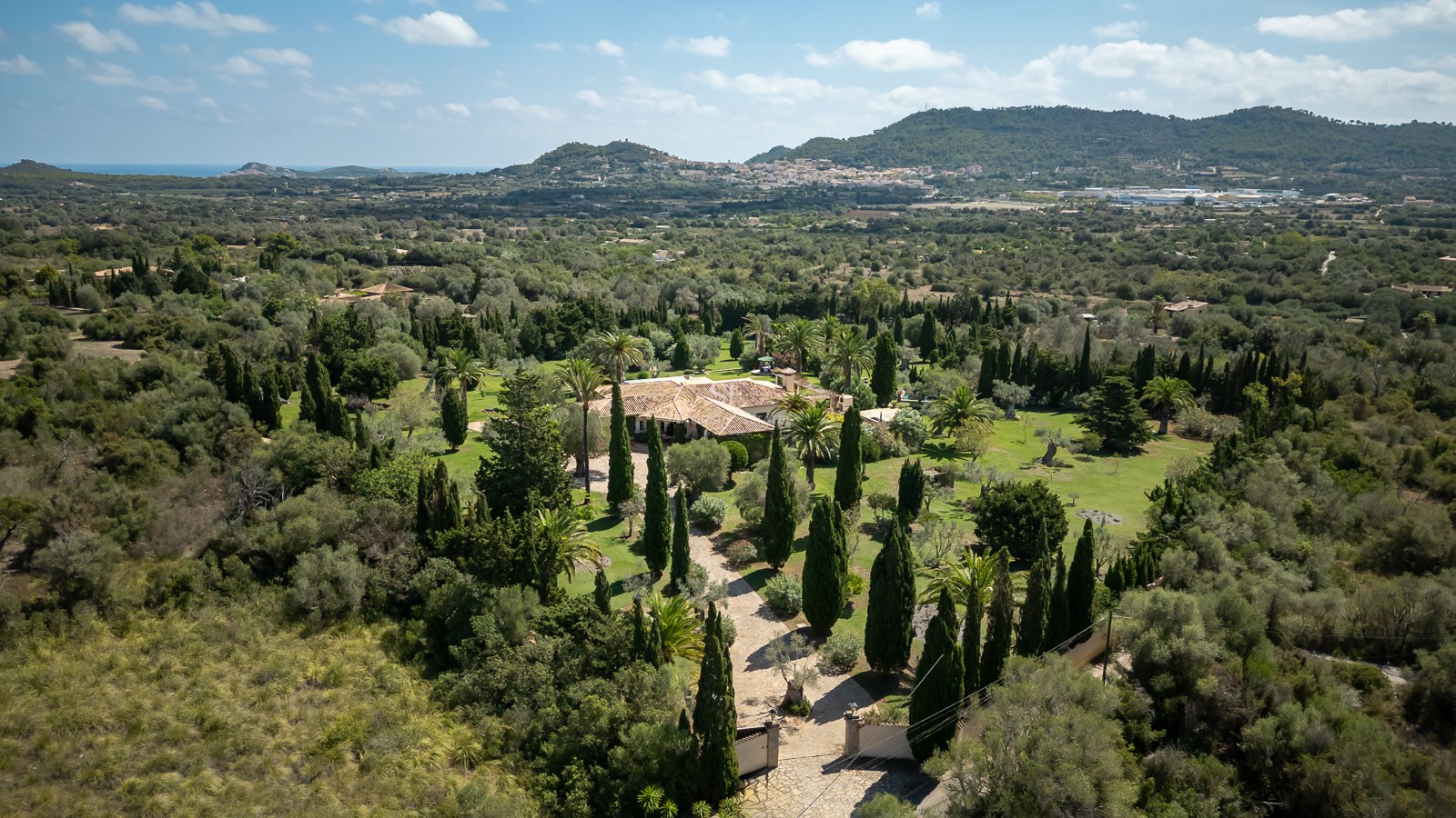 Vue aérienne d'une villa de luxe avec toit en terre cuite entourée de jardins verdoyants et de montagnes à Majorque.