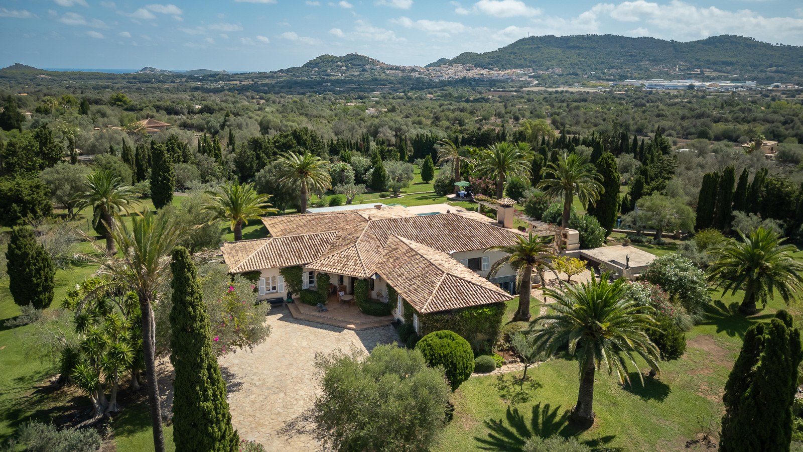 Luftaufnahme einer herrschaftlichen mediterranen Villa mit Terrakotta-Dächern inmitten einer üppigen Parkanlage.