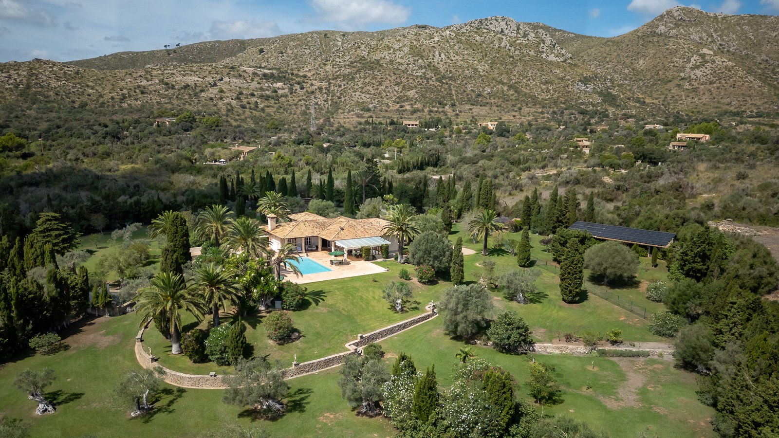 Vue aérienne d'une villa méditerranéenne avec piscine, grands jardins et montagnes en arrière-plan.
