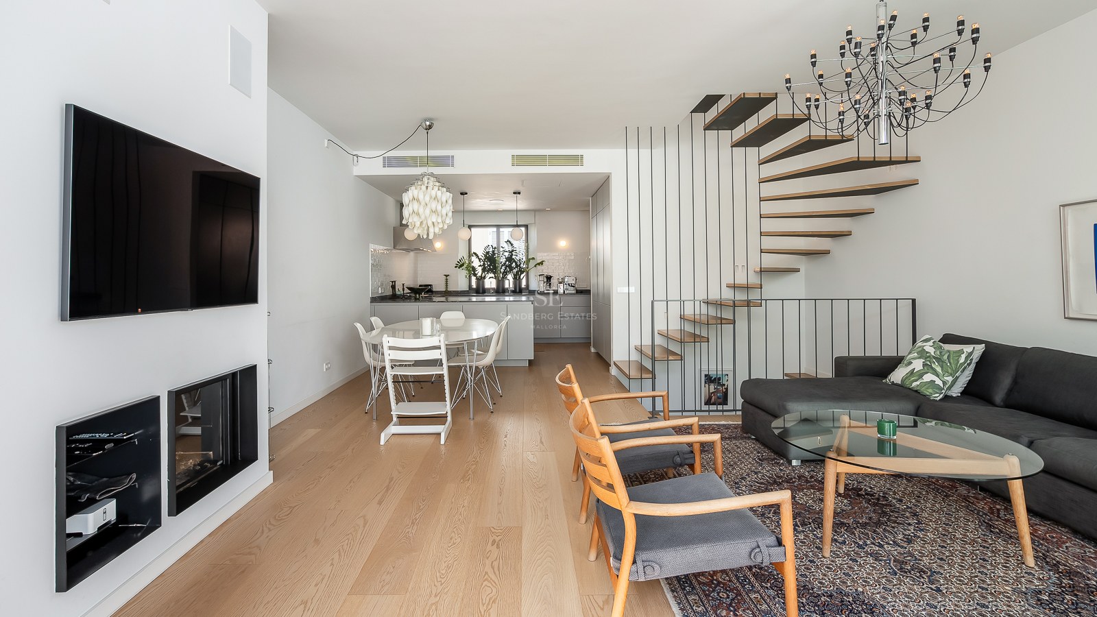 Espace de vie et salle à manger lumineux avec parquet en chêne clair, escalier suspendu moderne et cuisine intégrée.