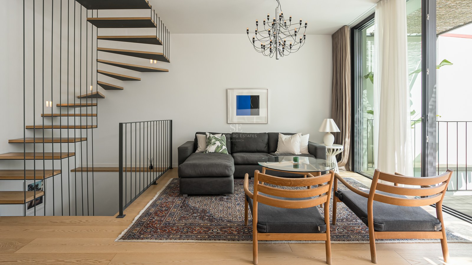Salon contemporain avec canapé gris, escalier en colimaçon en bois et grandes baies vitrées.