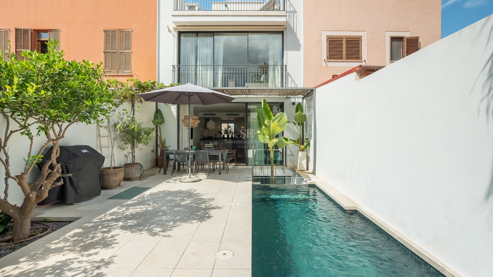 Cour extérieure moderne avec piscine, coin repas sous un parasol et murs blancs.