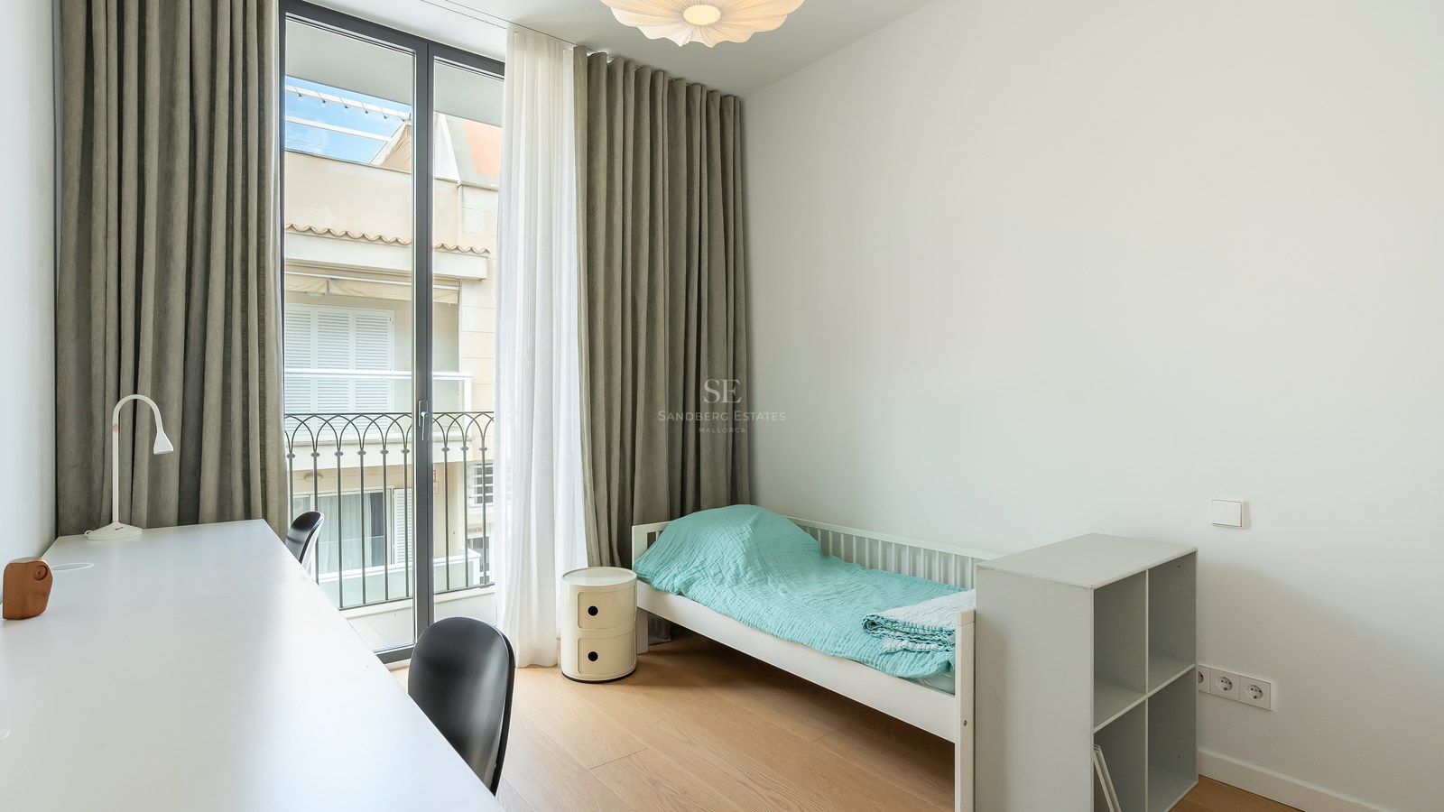 Chambre minimaliste avec un lit simple, un bureau blanc, de grandes portes vitrées et un parquet en bois clair.