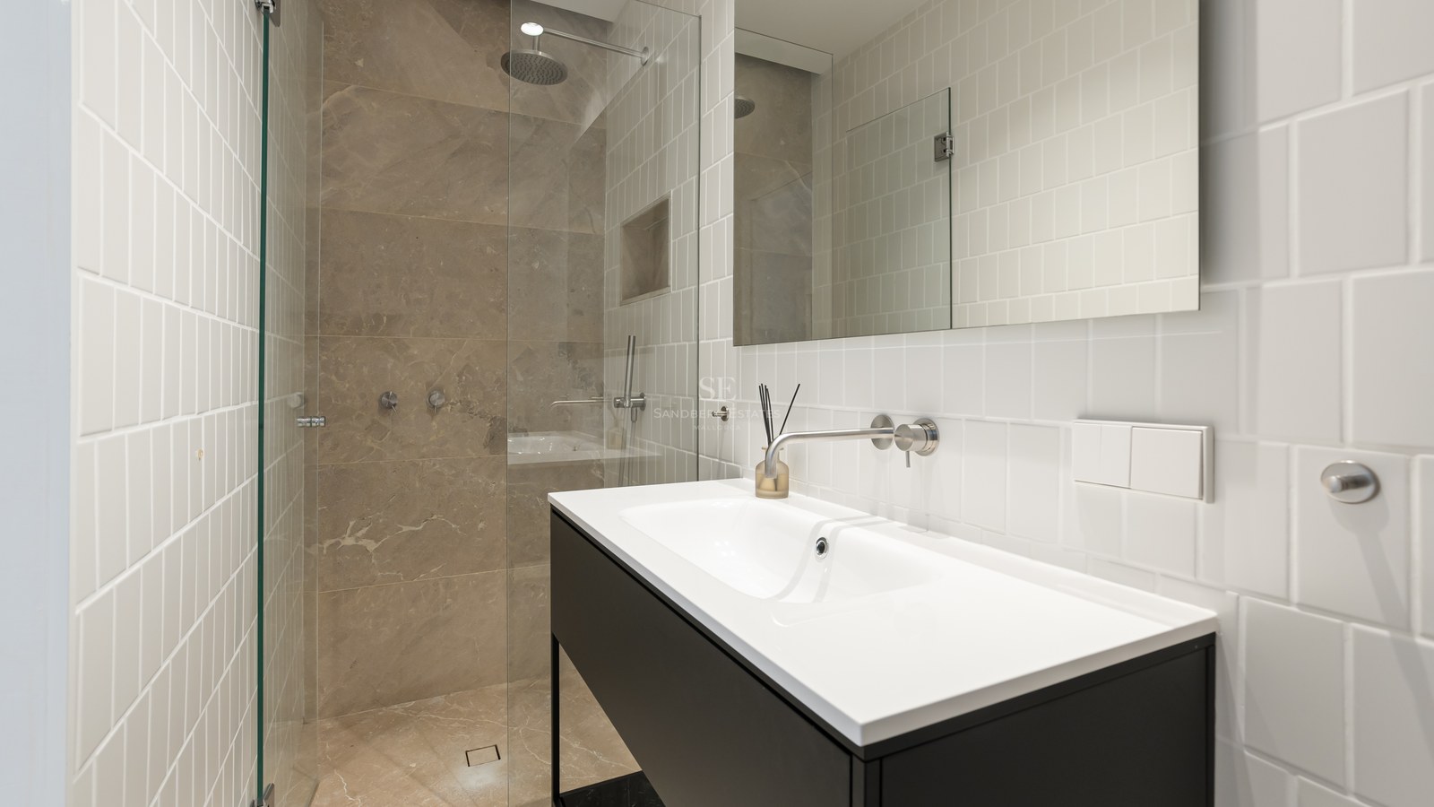 Salle de bain moderne avec carrelage blanc, meuble noir et douche à l'italienne avec parois en verre.