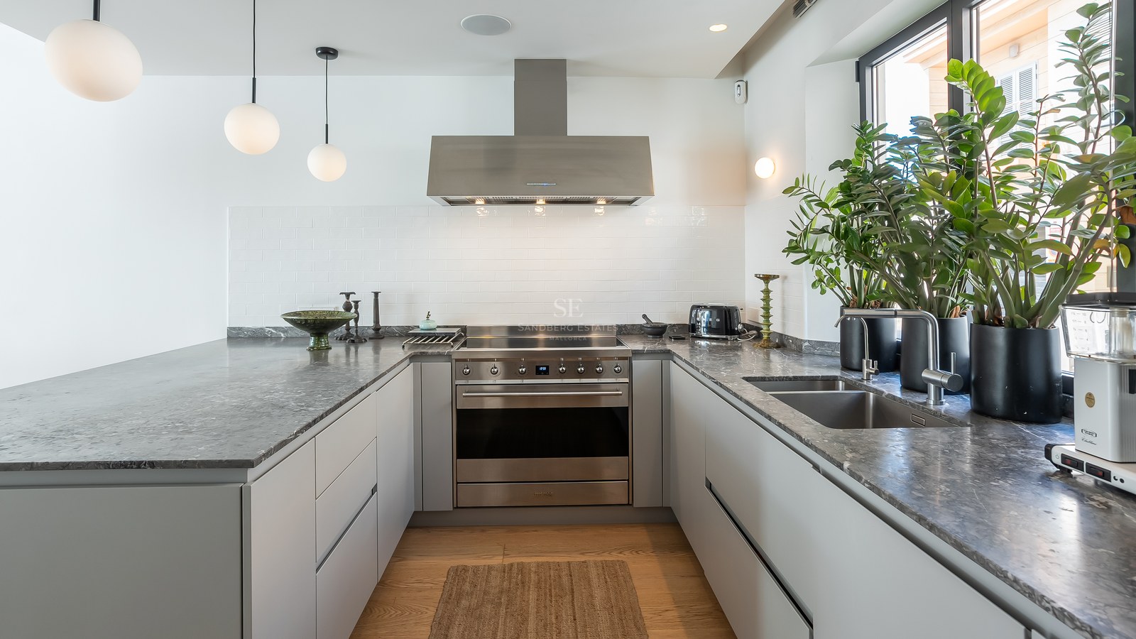 Cuisine moderne en U avec plans de travail en pierre grise, appareils en inox et lumière naturelle.