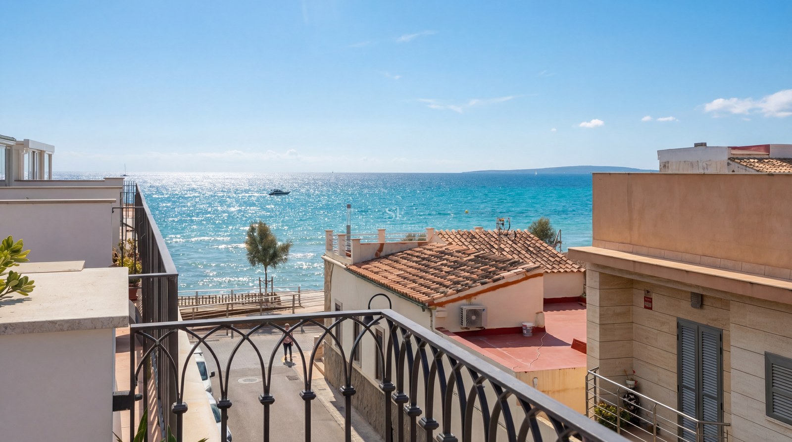 Vue depuis un balcon en fer forgé surplombant des toits en terre cuite vers la mer turquoise et l'horizon.