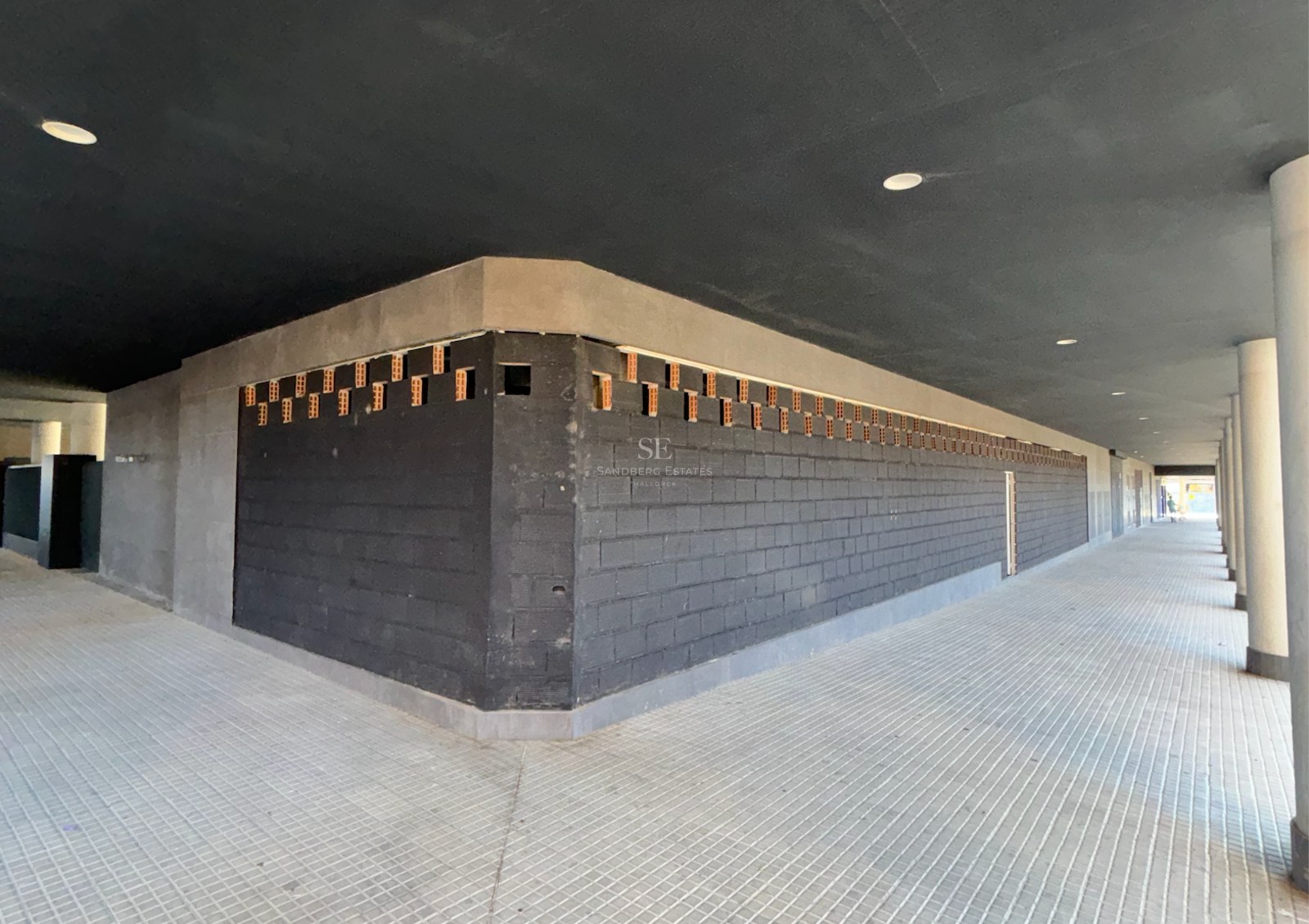 Covered walkway featuring dark block walls, concrete pillars, and recessed ceiling lighting.