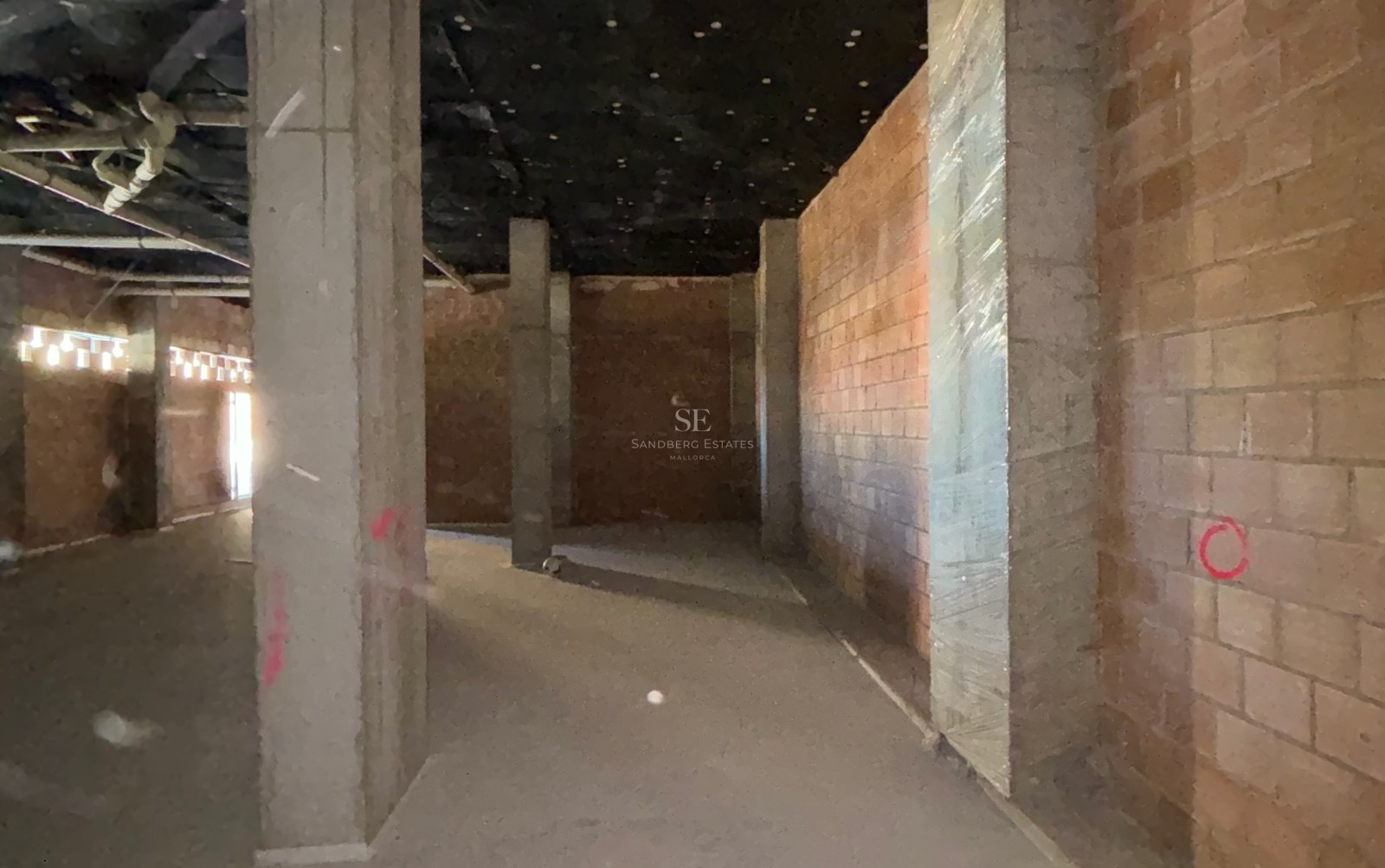 Interior view of a spacious underground parking area in its early construction phase with concrete pillars and brick walls.