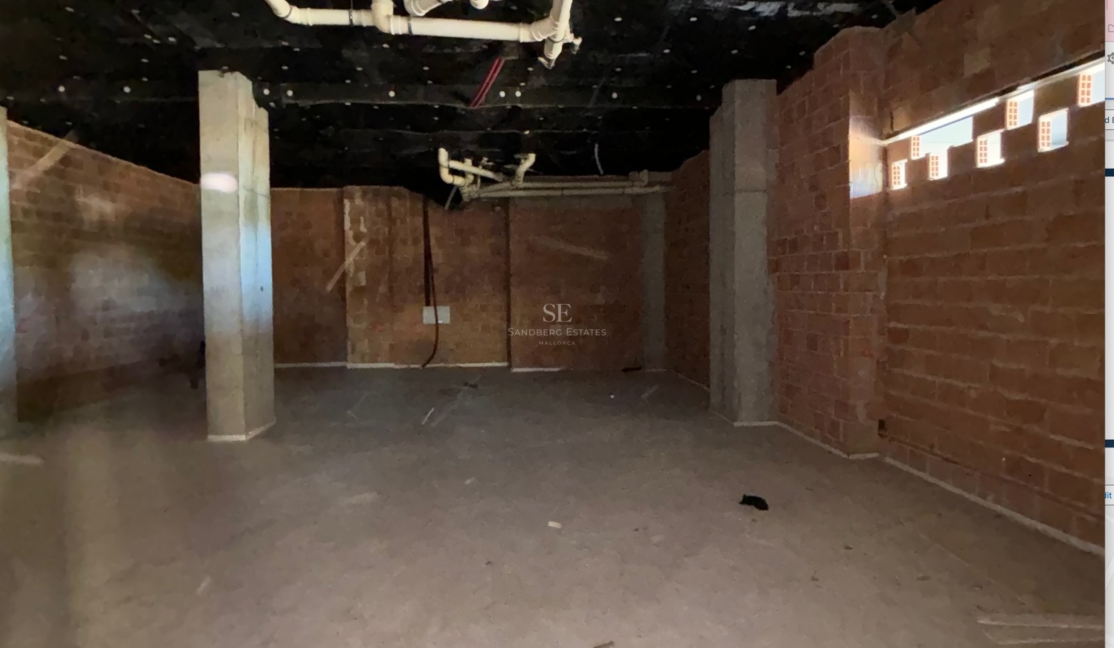 Interior room under construction with red brick walls, concrete pillars, and exposed ceiling pipes and insulation.