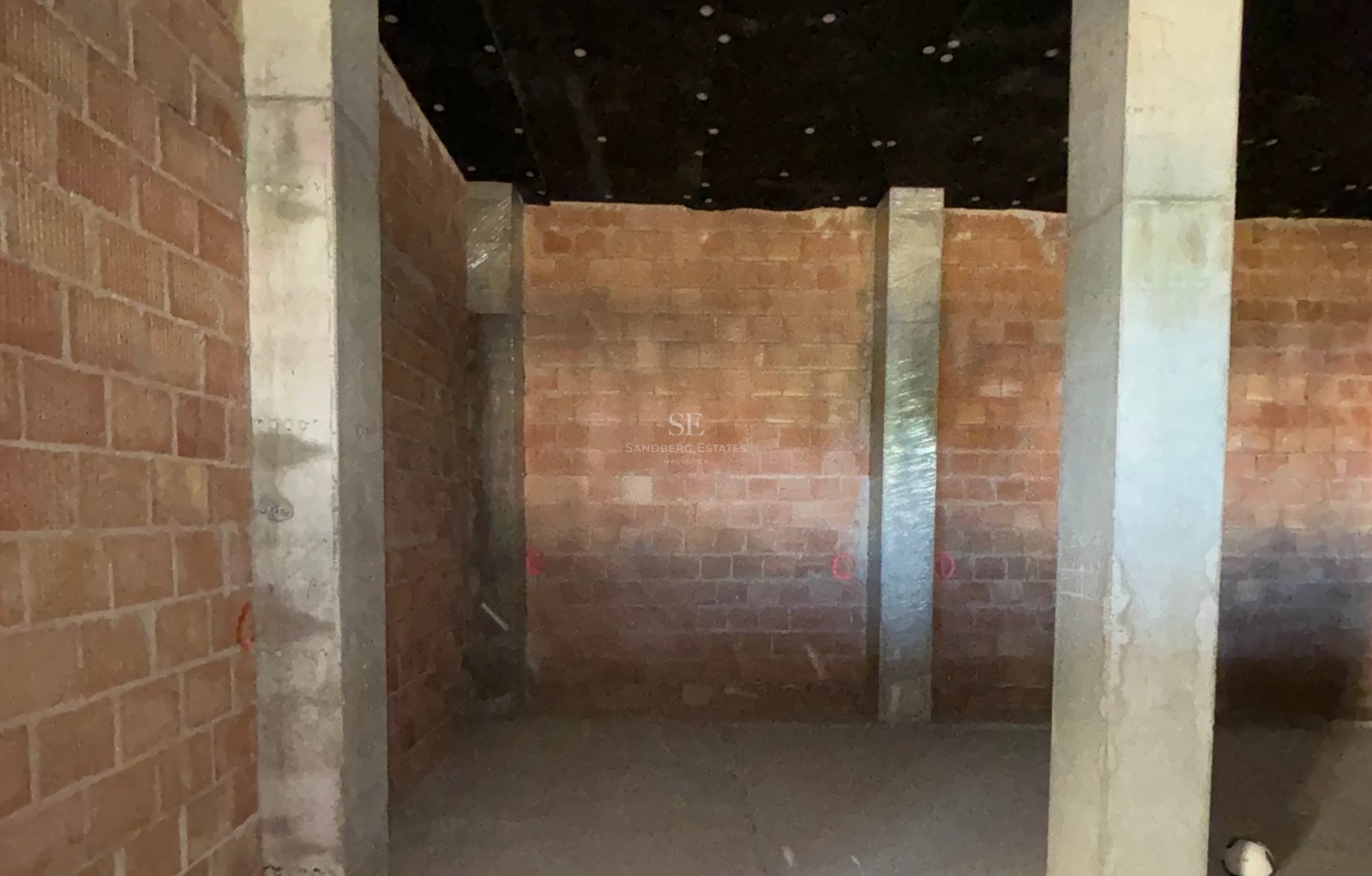 Interior view of a construction site featuring raw brick walls, concrete pillars, and an insulated ceiling.