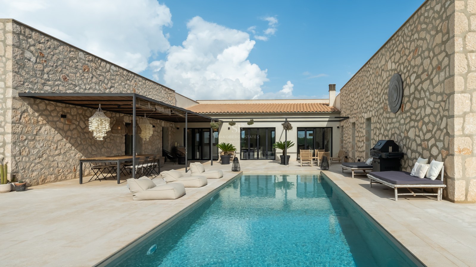 Cour centrale d'une villa de luxe en pierre avec piscine rectangulaire et espace repas ombragé.