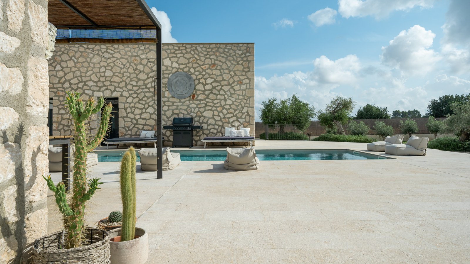 Piscine privée entourée d'une terrasse en pierre calcaire, murs en pierre sèche et salon d'été avec plantes exotiques.
