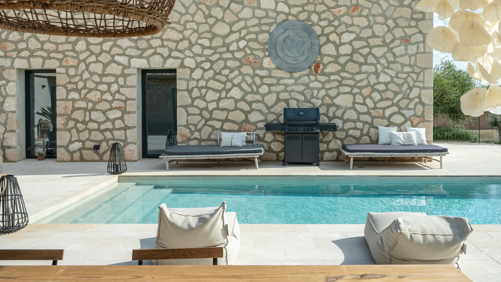 Piscine de luxe avec mur en pierre naturelle, barbecue intégré et mobilier de détente moderne.