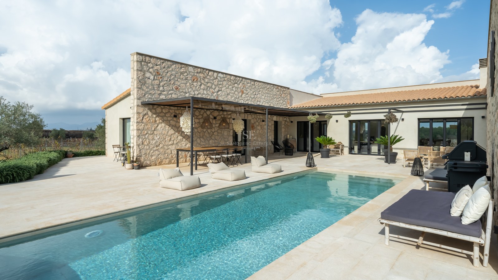 Piscine de luxe à côté d'une façade en pierre naturelle avec coin repas sous pergola et bains de soleil.