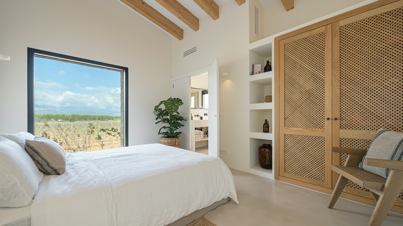Chambre moderne avec poutres en bois, grande fenêtre donnant sur un vignoble et armoires en cannage.