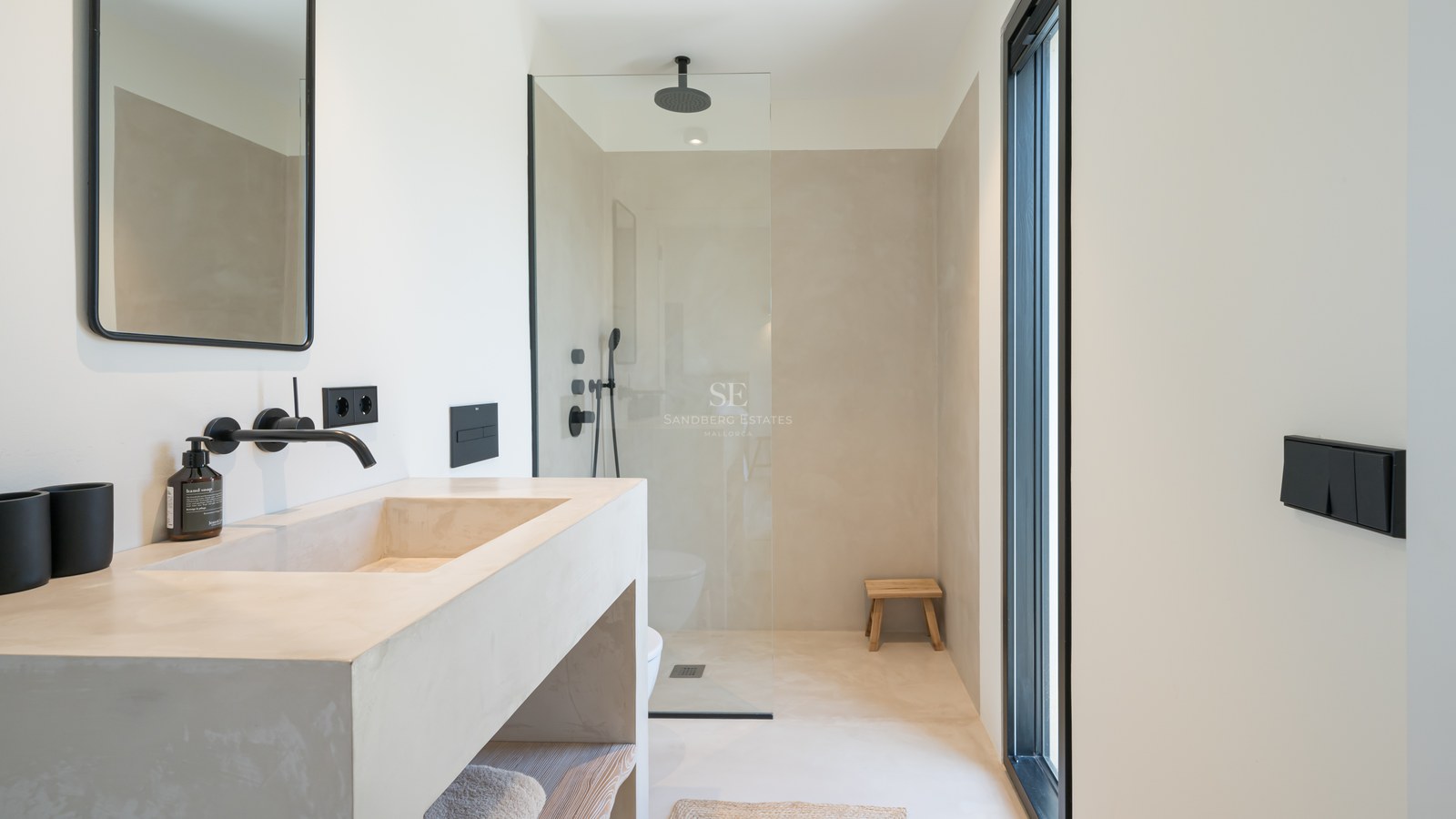 Salle de bain moderne avec lavabo en microciment, robinetterie noir mat et douche à l'italienne vitrée.