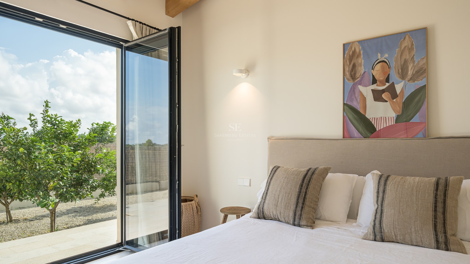 Chambre moderne avec lit en lin, poutres en bois et baies vitrées ouvrant sur un jardin avec un citronnier.