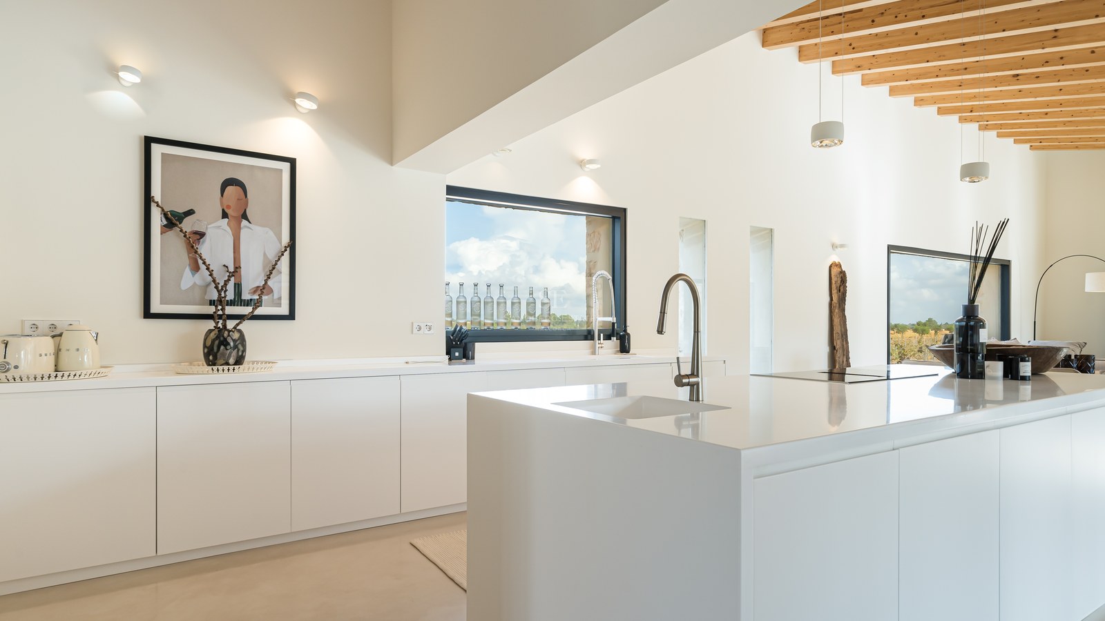 Cuisine blanche minimaliste avec îlot, plans de travail en quartz et plafond en poutres de bois naturel.