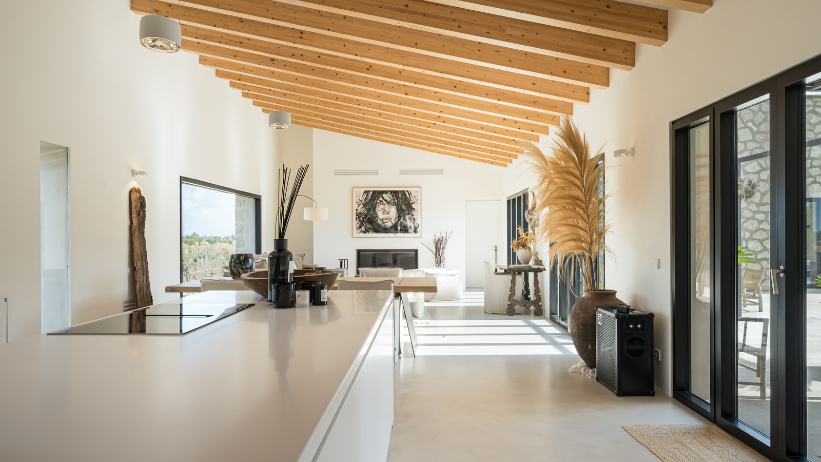 Cuisine moderne avec îlot blanc, hauts plafonds en bois et grandes baies vitrées donnant sur l'extérieur.