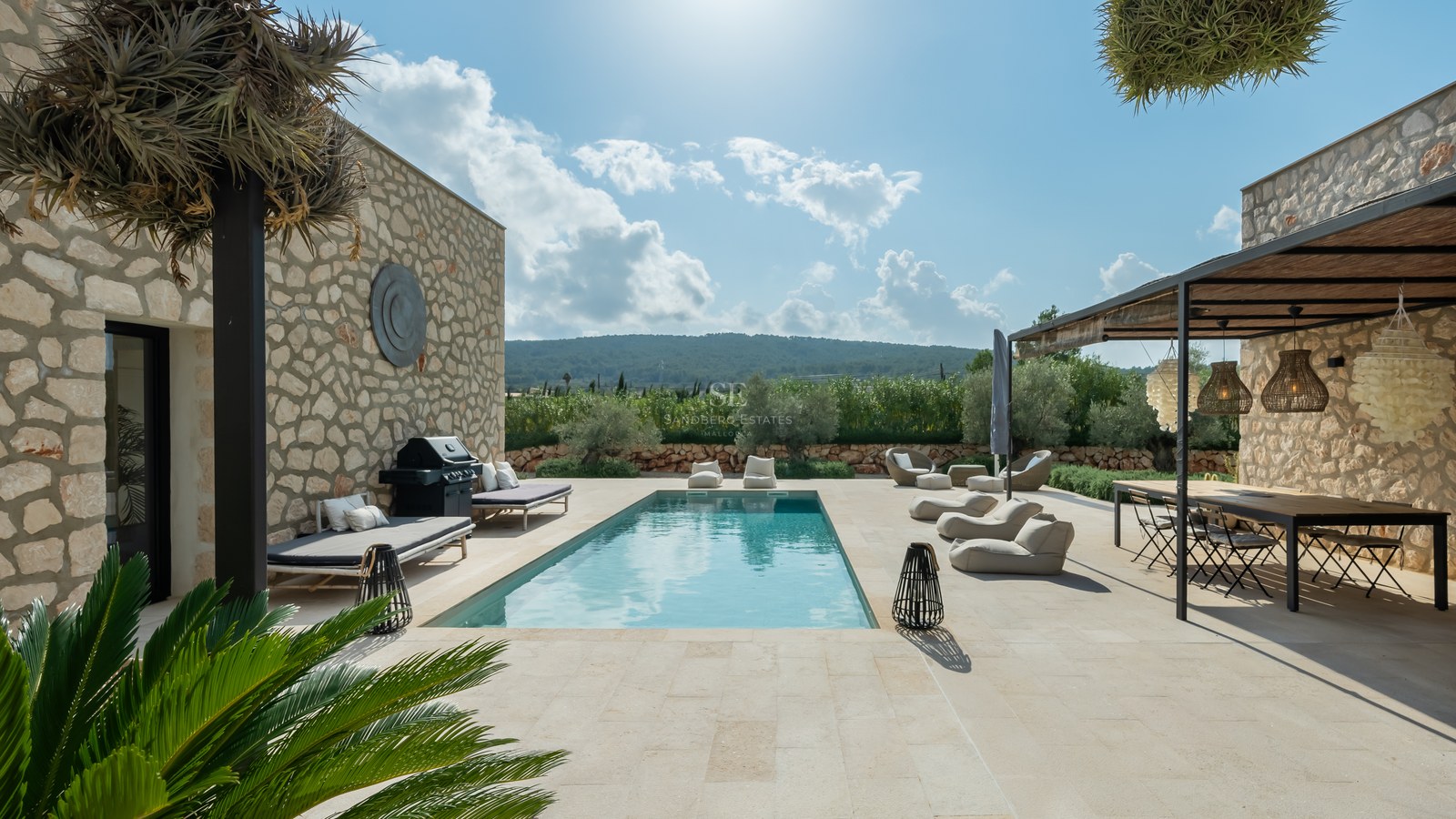 Piscine rectangulaire turquoise entourée d'une terrasse en pierre, coin repas extérieur et murs en pierre naturelle.